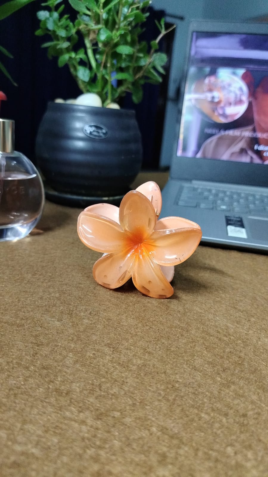 Serraw orange Hawaiian flower hair clip with translucent petals on a brown surface near a laptop