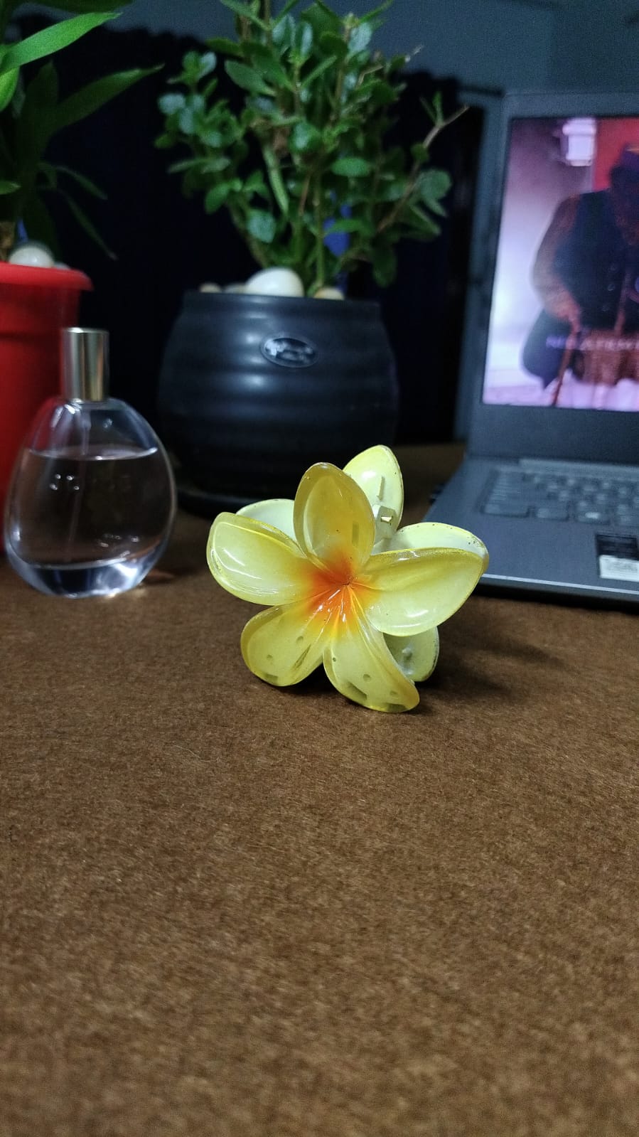 Serraw yellow Flower hair clip shaped like a yellow plumeria flower with orange center on a brown surface